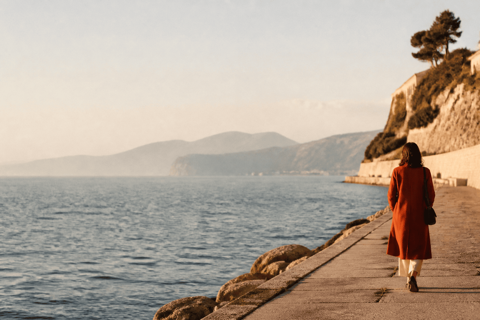 A woman in an orange coat walking beside the sea